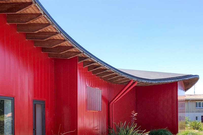 Toit en forme de vague et façade rouge du dojo Pierre de Coubertin réalisé par l'agence Bulle Architectes à la Teste-de-Buch.