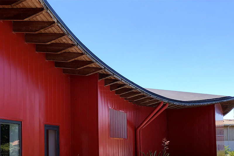 Wave-shaped roof and red facade of the Pierre de Coubertin dojo designed by Bulle Architectes at La Teste-de-Buch.