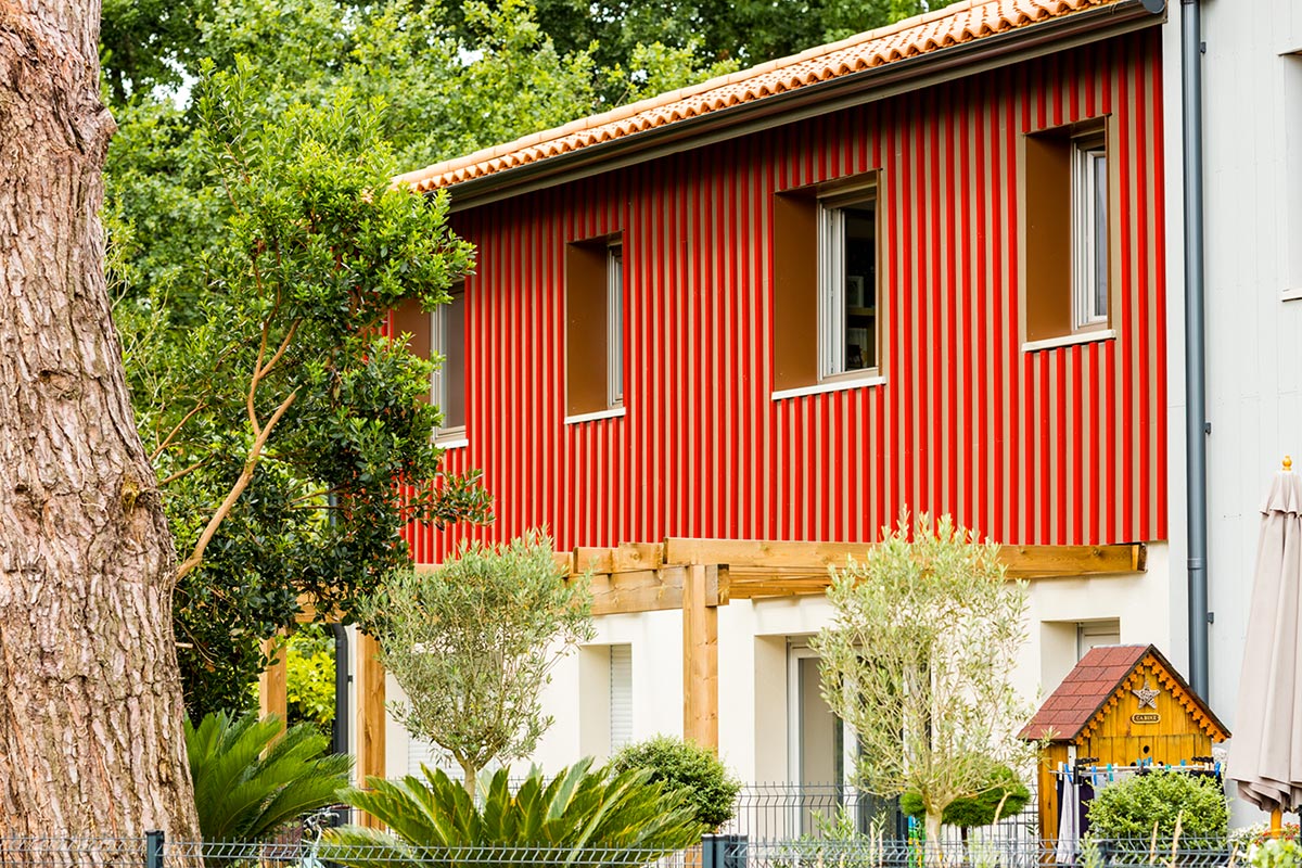 Zoom sur façade au bardage en bois rouge d'un habitat collectif faisant partie de la résidence L'Orée du Parc réalisée au Teich par l'agence Bulle Architectes.