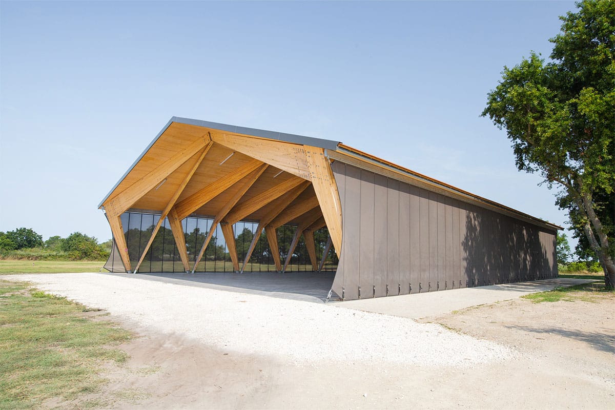Vue depuis l'extérieur de l'ensemble de la halle couverte en bois du Teich réalisée par l'agence Bulle Architectes.