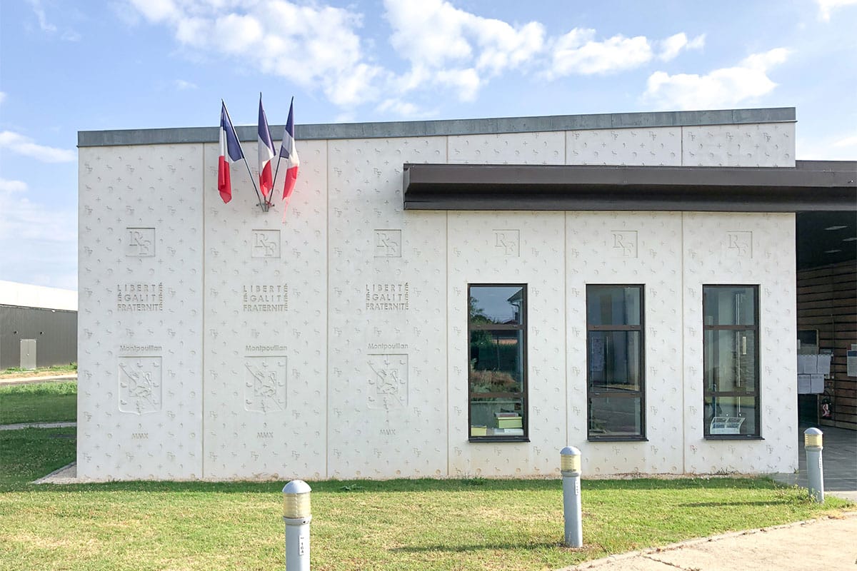 Côté gauche de la façade principale en béton matricé avec le drapeau français de la mairie de Montpouillan réalisée par l'agence Bulle Architectes.