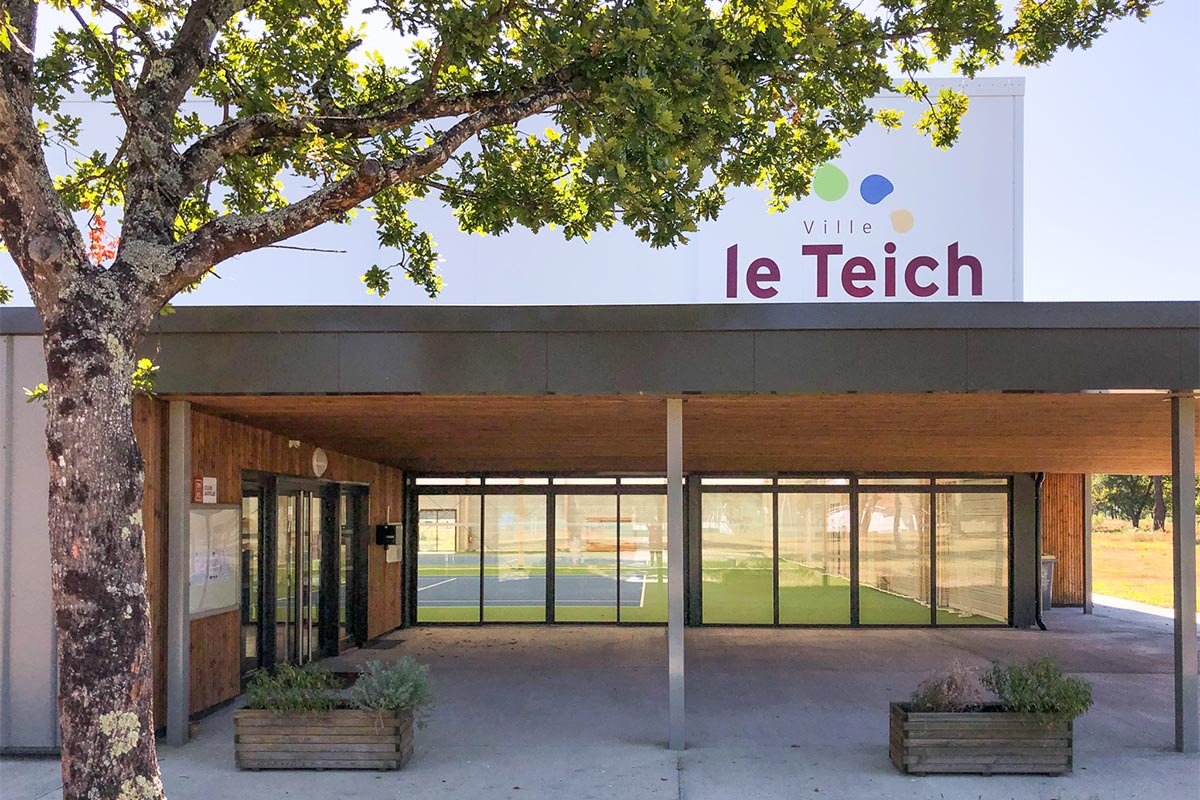 Vue de l'entrée principale avec le logo de la ville du Teich sur la façade du club de tennis du Teich réalisé par l'agence Bulle Architectes.