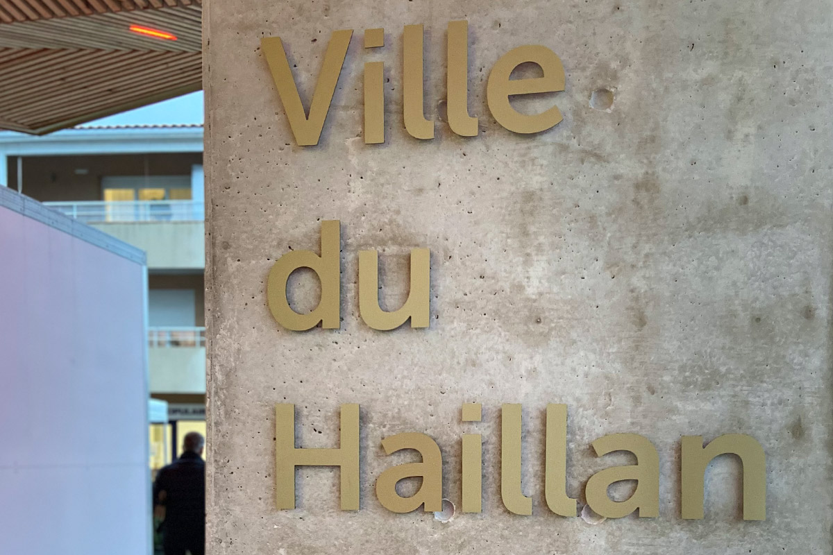 Lettrage doré présent sur le totem en béton de la nouvelle halle couverte du Haillan réalisée par l'agence bordelaise Bulle Architectes.